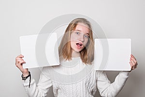 Positive girl holds a blank poster for text. Cute schoolgirl with a smile holds a white sheet for text