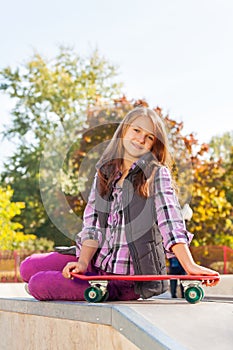 Positive girl holds skateboard sits on ground