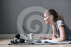 Positive girl with laptop surfing Internet, laying on the floor.