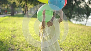 Positive girl playing with multicolored balloons on sunny day in spring summer park. Portrait of cheerful brunette