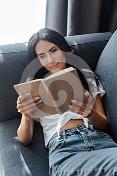 Positive girl reading book on sofa in living room