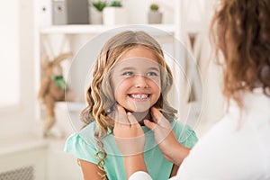 Positive girl staring at female doctor who checking her tonsils