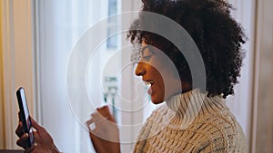 Positive girl using smartphone at home. Curly smiling lady trying mobile phone