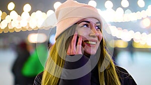 Positive girl in winter outfit talking on phone near skating rink