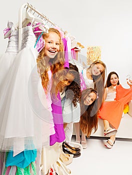 Positive girls during shopping behind hangers