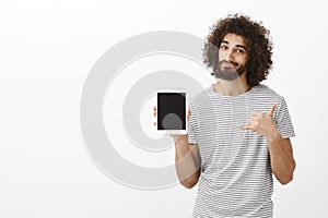 Positive good-looking male surger in striped t-shirt, showing white digital tablet and making urban gesture, advicing