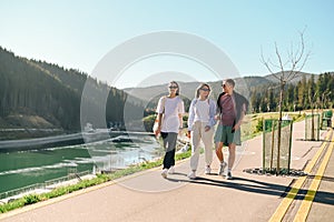 A positive group of friends of tourists in casual clothes walk around the mountain resort in summer and communicate with smiles on