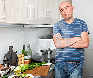 Positive guy stands proudly in kitchen hands clasped