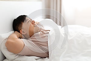 Positive happy asian man lying in bed at home, dreaming