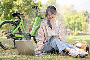 A positive, happy young Asian female college student is doing homework in a campus park