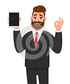 Positive happy young business man showing or holding blank screen of tablet computer display and gesturing, making okay, ok sign.