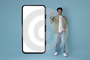 Positive hindu guy pointing at huge phone with blank screen