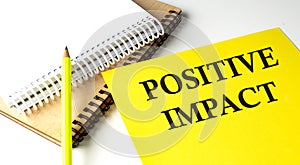 POSITIVE IMPACT text written on a yellow paper with notebook