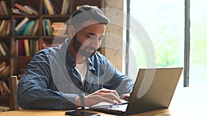 Positive Indian male freelancer looks at the laptop monitor