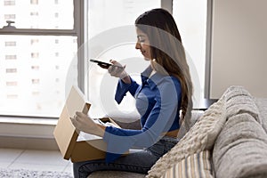 Positive Indian woman using mobile phone over open cardboard box