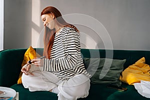 Positive injured young woman with broken right arm wrapped in white gypsum bandage applying cosmetic on face with