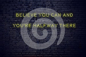 Positive inspiring quote on neon sign against brick wall believe you can and youre halfway there