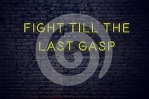 Positive inspiring quote on neon sign against brick wall fight till the last gasp