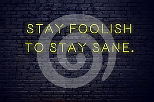 Positive inspiring quote on neon sign against brick wall stay foolish to stay sane