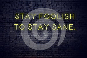 Positive inspiring quote on neon sign against brick wall stay foolish to stay sane photo