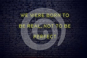 Positive inspiring quote on neon sign against brick wall we were born to be real not to be perfect