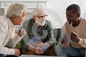 Positive interracial pensioners playing cards at