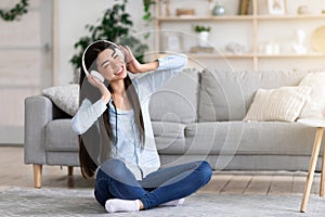 Positive korean girl enjoying music in wireless headphones while relaxing at home