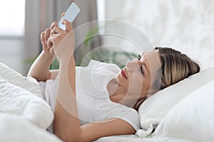 Positive lady laying in bed alone, using mobile phone
