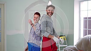 Positive laughing couple posing in new house in paper hats having fun renovating living room. Portrait of happy loving