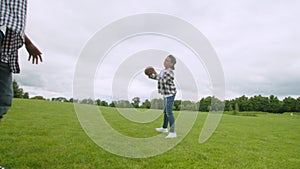 Positive little boy throwing american football ball to dad outdoors