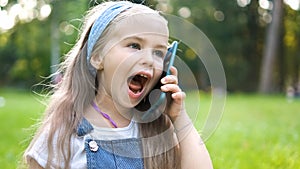 Positive little child girl having conversation on her mobile phone in summer park. Young female kid talking on sellphone