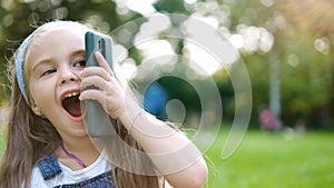 Positive little child girl having conversation on her mobile phone in summer park. Young female kid talking on sellphone