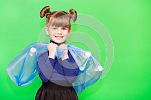 Positive little ecologist girl holding trash bags with plastic bottles isolated on green background
