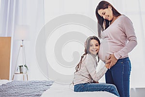 Positive little girl keeping her head at mothers belly