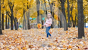 Positive little girl playing in the autumn park. Happy emotional child catches maple leaves and laughs. active holiday in autumn.