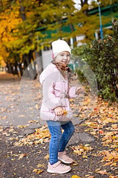 Positive little girl playing in the autumn park. Happy emotional child catches maple leaves and laughs. active holiday in autumn.