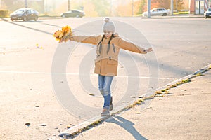 Positive little girl walking on the curb with maple leaves in her hand and trying to keep her balance