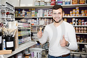 positive male customer examining various types of brushes in paint store