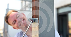 Positive male houseworker paints new railings on balcony