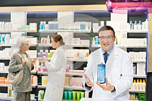 Positive male pharmacist in medical uniform posing with intimate hygiene product in hands in pharmacy
