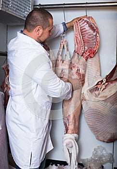 Positive male shop staff cutting sirloin at top