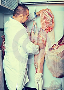 Positive male shop staff cutting sirloin at top