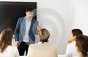 Positive male trainer, conducting advanced training courses to office employees sitting at desks in auditory