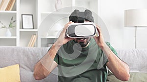 Positive male wearing VR goggles while sitting on couch