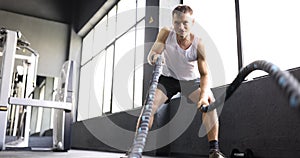 Positive man does effective exercise with heavy battle ropes