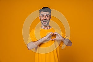 Positive man doing heart gesture and looking at camera while standing isolated