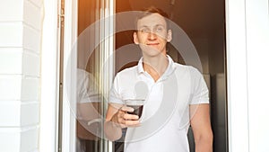 Positive man drinks cup of coffee standing on balcony