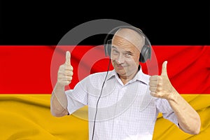Positive man in headphones against the background of the national flag of Germany on delicate shiny silk with soft draperies,