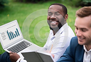 Positive man sitting on the grass with his colleague