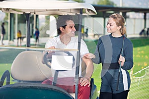 Positive man and woman golfers riding golf cart